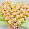 Heart-shaped bouquet of pale peach roses wrapped in green paper