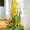 Tall yellow floral arrangement with sunflowers in a white pedestal vase