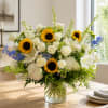 Large bouquet of white roses, sunflowers, and blue flowers in a glass vase