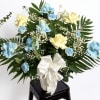 Blue and yellow rose arrangement with white ribbon in a vase
