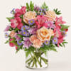Mixed bouquet of pink and peach flowers in a clear glass vase