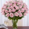 Pink roses arranged in a clear glass vase with a gift box and champagne flutes nearby