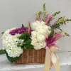 Basket arrangement of white roses, hydrangeas, and pink lilies with ribbon