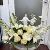 White floral arrangement with roses, lilies, and a small religious statue