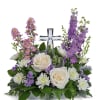 White roses and purple flowers arranged around a clear glass cross