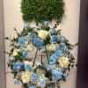 Blue and white rose wreath on a stand beneath a green foliage panel