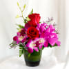 Red roses and purple orchids in a green glass vase with a pink ribbon