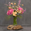 Tall bouquet of pink hydrangeas, peach roses, and lavender flowers in a glass vase