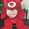 Large red teddy bear holding a heart pillow that says I Love You