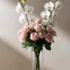 Pink roses and white orchids arranged in a clear glass vase.
