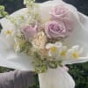 Handheld bouquet of pale pink and white flowers wrapped in white paper