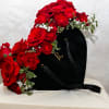 Heart-shaped black box topped with red roses and small white flowers