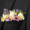 Floral boutonniere with white daisies, purple blooms, and cream rose buds on a black jacket