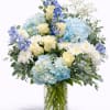 Blue hydrangeas, ivory roses and white mums in a clear glass cylinder vase