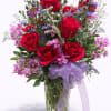 Bouquet of red roses and purple flowers in a glass vase with a lavender ribbon