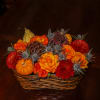 Basket arrangement with orange and red flowers, pumpkins, and thistle-like accents