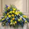 Large floral spray with yellow roses, blue flowers, and palm fronds