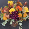 Fall bouquet with yellow roses, orange spray roses, and purple chrysanthemums in a decorative container