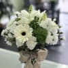 White floral bouquet in a clear glass vase with a burlap bow