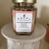 A glass jar of flower bath salts with a gold lid on a white pedestal