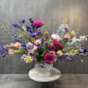 Large mixed bouquet of pink, purple, and blue flowers in a white pedestal vase