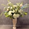 Tall floral arrangement in a pedestal vase with white, peach, and blue blooms