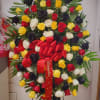 Large standing rose arrangement in red, yellow, white, and black with a red bow