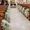 White floral arrangements line the aisle of a church interior.
