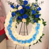 Blue and cream rose arrangement above a white-and-blue floral wreath on a stand