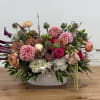 Low oval arrangement of pink dahlias, roses, calla lilies and mixed blooms in a white ceramic vase.