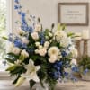 Blue delphinium, white lilies, and cream roses in a white pedestal vase