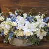 White lilies and roses in a low basket beside a memorial urn and framed portrait