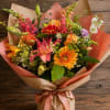 Mixed bouquet of orange, pink, and white flowers wrapped in brown paper