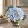 Blue hydrangea bouquet in a clear glass vase with round eucalyptus leaves