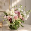 Pastel bouquet of roses, carnations, and white blooms in a glass bowl vase