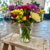 Mixed bouquet of purple, red, yellow, and white flowers in a glass jar vase
