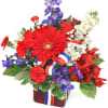 Red, white, and blue floral arrangement in a red glass vase with ribbon