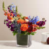 Colorful bouquet of roses, delphinium, and snapdragons in a square glass vase