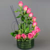Pink roses arranged in a green round vase with decorative wire accents
