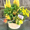 Basket of yellow flowering plants with tall plumes and a yellow bow on a glass table