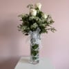 White roses and baby's breath in a tall glass vase with a white ribbon