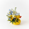 Yellow duck-shaped container holding blue, white, and yellow flowers