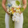 Bride holding a cascading bouquet of white, peach, yellow, and blue flowers