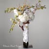 Tall floral arrangement with white orchids and pale blossoms in a glass vase