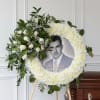 White floral funeral wreath on an easel with a portrait in the center
