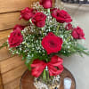 Red roses arranged in a glass vase with baby's breath and a red ribbon.