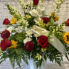 Red roses, sunflowers, and white flowers in a white vase with a ribbon