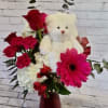 Red flowers arranged with a white teddy bear in a vase