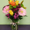 Bouquet of pink gerbera daisies, yellow roses, and orange lilies in a glass vase