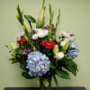 Mixed bouquet in a glass vase with blue hydrangeas, lilies, and gerbera daisies